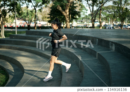 Female runner jogging down concrete steps during outdoor workout in urban park with morning light Female runner jogging down concrete steps during outdoor workout in urban park with morning light 134916136