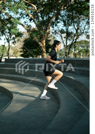Female runner jogging down concrete steps during outdoor workout in urban park with morning light 134916138