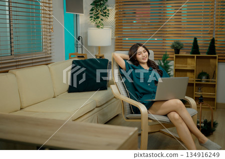 Young woman sitting on armchair and relax with laptop computer Young woman sitting on armchair and relax with laptop computer 134916249