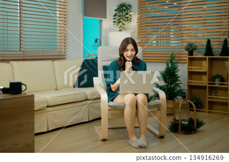 Young woman sitting on armchair and using laptop computer Young woman sitting on armchair and using laptop computer 134916269