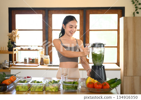 Woman blending fresh green vegetables in a blender to make a healthy green smoothie, representing clean eating and wellness lifestyle. Woman blending fresh green vegetables in a blender to make a healthy green smoothie, representing clean eating and wellness lifestyle. 134916350