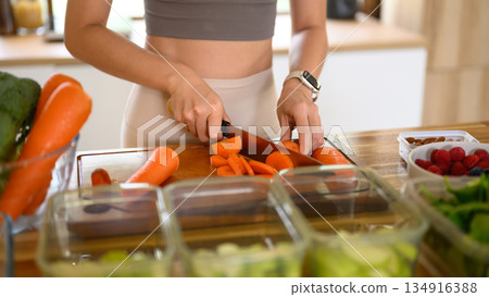 Closeup of young female hands chopping fresh orange carrot on board while in modern kitchen 134916388