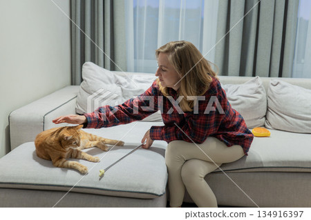 Woman caresses bright orange feline, Relaxed woman softly pets lively orange feline in peaceful setting, Calm woman enjoys soothing strokes on her bright orange pet in tranquil environment 134916397
