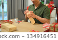 Photo set Man wrapping Christmas gifts at home with scissors and festive decorations 134916451