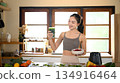 Happy young woman holding a glass of fresh green smoothie in her kitchen, celebrating a healthy lifestyle 134916464