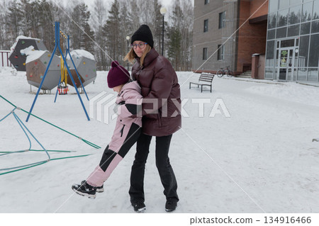 white caregiver lifting daughter midspin on snowy park, maroon puffer and pink snowsuit contrast, motion blur of boots and swinging legs, laughter and energetic play, playground equipment and trees white caregiver lifting daughter midspin on snowy park, maroon puffer and pink snowsuit contrast, motion blur of boots and swinging legs, laughter and energetic play, playground equipment and trees 134916466