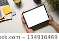 Woman hand holding tablet on office desk workspace with, pen, laptop, flower and hot coffee cup on white table 134916469