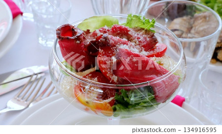 Roasted beef slices nestling over crisp lettuce, garnished with cherry tomatoes and parmesan, presenting gourmet salad composition in clear glass serving bowl Roasted beef slices nestling over crisp lettuce, garnished with cherry tomatoes and parmesan, presenting gourmet salad composition in clear glass serving bowl 134916595