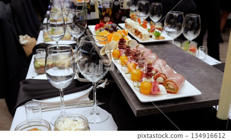 Wine glasses surrounding gourmet appetizers resting on dramatic black white checkered tablecloth, highlighting elegant catered dining experience Wine glasses surrounding gourmet appetizers resting on dramatic black white checkered tablecloth, highlighting elegant catered dining experience 134916612