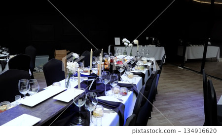 Sophisticated table setting featuring white carnations, candles, wine glasses, plates, black napkins, preparing elegant ambiance for corporate gathering or special event Sophisticated table setting featuring white carnations, candles, wine glasses, plates, black napkins, preparing elegant ambiance for corporate gathering or special event 134916620