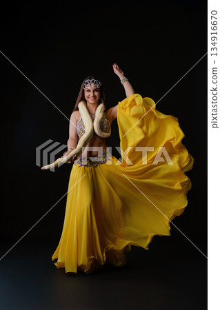 Woman dances with snake in vibrant costume in a studio setting during an evening performance Woman dances with snake in vibrant costume in a studio setting during an evening performance 134916670
