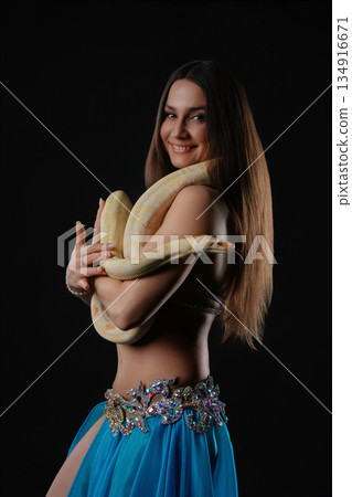 Woman performs dance while holding a snake in a dark setting during an evening event Woman performs dance while holding a snake in a dark setting during an evening event 134916671