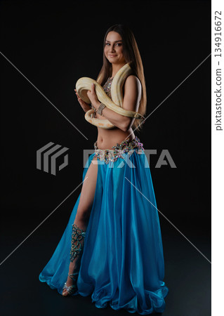 Woman doing dance with snake indoors at night wearing blue outfit and holding snake Woman doing dance with snake indoors at night wearing blue outfit and holding snake 134916672