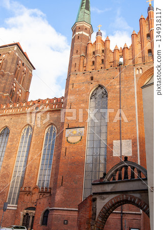 Historic brick church with tall tower under blue sky in city setting 134918117
