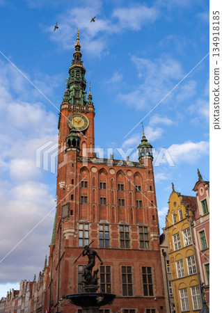 Gdansk clock tower stands tall over buildings and a fountain under blue sky Gdansk clock tower stands tall over buildings and a fountain under blue sky 134918185