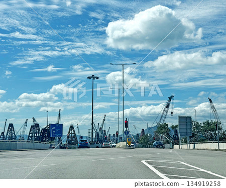 Construction cranes and vehicles on a busy road under a cloudy blue sky Construction cranes and vehicles on a busy road under a cloudy blue sky 134919258