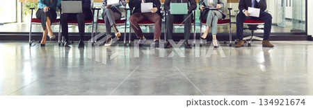 Legs of unrecognizable business people sitting on chairs in a row with resumes and laptops. 134921674