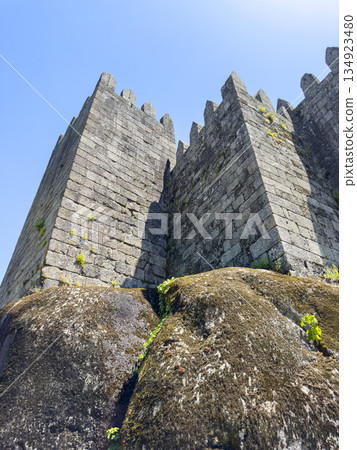 Bottom view of Guimaraes Castle in Portugal with massive stone walls and battlements rising above 134923480