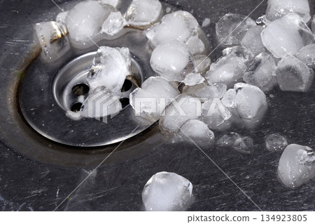 Melting ice cubes dripping down a sink plug drain silver metal basin 134923805