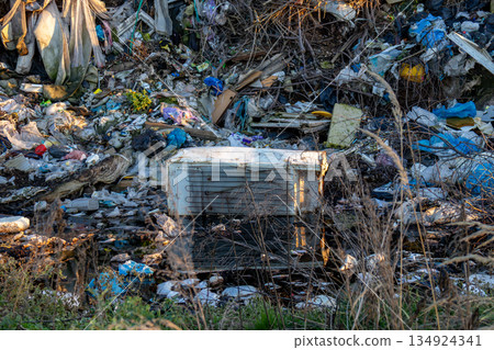 Garbage and waste materials fill a landfill site with a discarded appliance surrounded by pollution and debris in the bright daylight Garbage and waste materials fill a landfill site with a discarded appliance surrounded by pollution and debris in the bright daylight 134924341