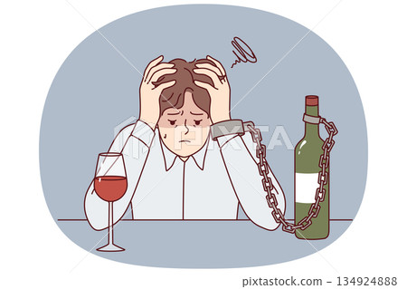 Man suffering from alcohol addiction is chained to bottle of wine, sitting at table clutching head Man suffering from alcohol addiction is chained to bottle of wine, sitting at table clutching head 134924888