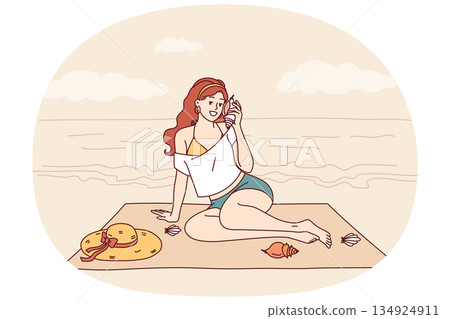 Woman sits on beach and listens to sound sea from shell, enjoying summer vacation at tropical resort 134924911