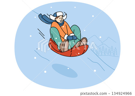 Teenage boy is relaxing at winter ski resort, sliding down snow-covered hill on inflatable sled Teenage boy is relaxing at winter ski resort, sliding down snow-covered hill on inflatable sled 134924966