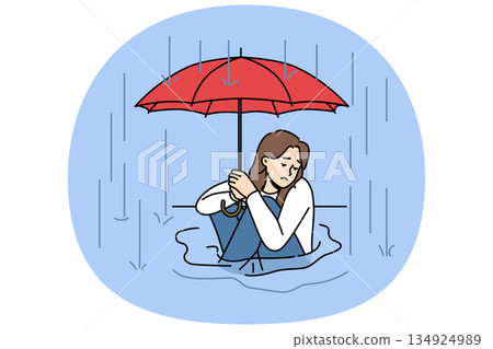 Woman sits in puddle in rain and holds umbrella over head, trying to escape autumn downpour 134924989