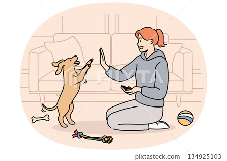 Woman trains dog while sitting on floor near sofa and giving food to puppy after following command 134925103