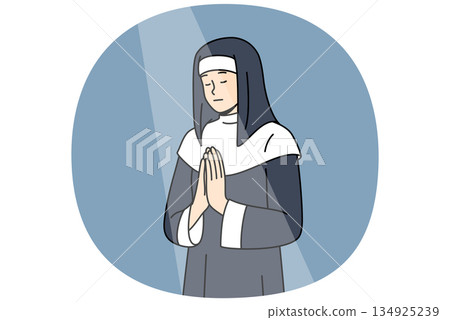 Nun prays to god with palms folded in front chest, standing under beam light in cathedral building 134925239