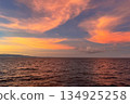 Vibrant orange yellow sunset over sea with boat wake in foreground, dark clouds and peaceful ocean seascape 134925258