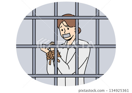 Woman hostage with hands tied standing inside prison cell and suffering due to restriction freedom Woman hostage with hands tied standing inside prison cell and suffering due to restriction freedom 134925361