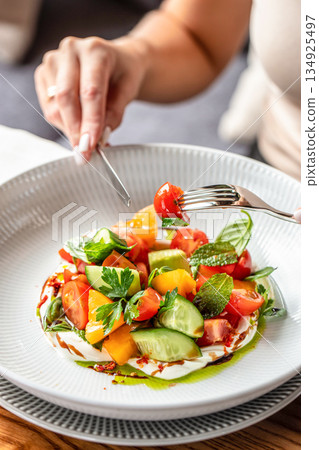 Woman eating fresh vegetable salad with tomatoes cucumber herbs and creamy cheese in restaurant, close up, copy space Woman eating fresh vegetable salad with tomatoes cucumber herbs and creamy cheese in restaurant, close up, copy space 134925497