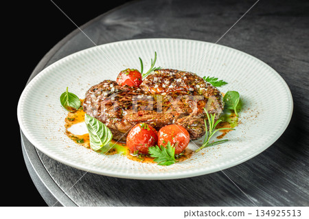 Grilled pork steak with herbs and cherry tomatoes served on white plate on dark table 134925513