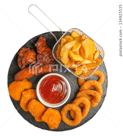 Fast food snack platter with chicken wings nuggets onion rings and potato wedges on black slate isolated on white background Fast food snack platter with chicken wings nuggets onion rings and potato wedges on black slate isolated on white background 134925535
