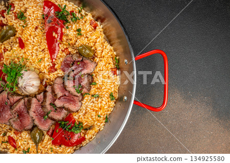 Top view of gourmet beef paella with roasted garlic and peppers in a traditional pan, with wide dark copy space on the right for text or design Top view of gourmet beef paella with roasted garlic and peppers in a traditional pan, with wide dark copy space on the right for text or design 134925580