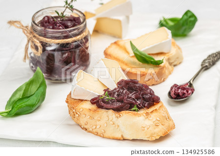 Bruschetta with brie cheese and caramelized red onion jam on toasted bread with basil on light background 134925586