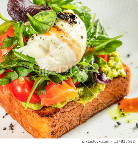 Avocado toast with poached egg, cherry tomatoes and fresh greens on toasted bread, close up, healthy breakfast concept 134925588