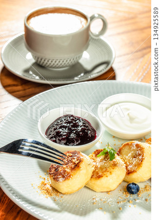 Cottage cheese pancakes with berry jam and sour cream served with coffee, close up breakfast dessert 134925589