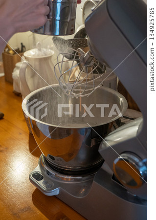 Hands sift flour into mixer bowl while preparing apple charlotte batter on wooden kitchen counter, capturing focused home baking moment 134925785