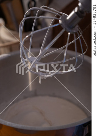 Mixer whisk covered with creamy apple charlotte batter hovers above a metal bowl, capturing a quiet home baking moment with soft smooth texture Mixer whisk covered with creamy apple charlotte batter hovers above a metal bowl, capturing a quiet home baking moment with soft smooth texture 134925791