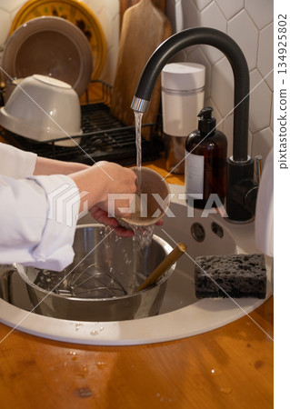 Hands rinse a ceramic cup under running water in a modern kitchen sink, with metal bowl, sponge, and soap creating a warm everyday home mood Hands rinse a ceramic cup under running water in a modern kitchen sink, with metal bowl, sponge, and soap creating a warm everyday home mood 134925802