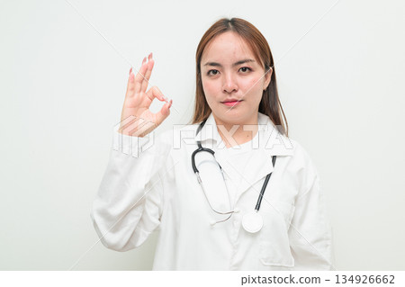 Portrait of young Asian female doctor against white background making OK sign gesture Portrait of young Asian female doctor against white background making OK sign gesture 134926662