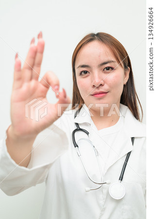 Portrait of young Asian female doctor against white background making OK sign gesture Portrait of young Asian female doctor against white background making OK sign gesture 134926664