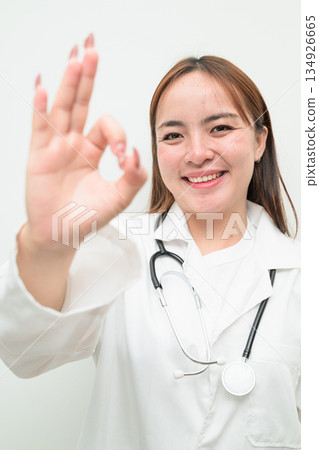 Portrait of young Asian female doctor against white background making OK sign gesture Portrait of young Asian female doctor against white background making OK sign gesture 134926665