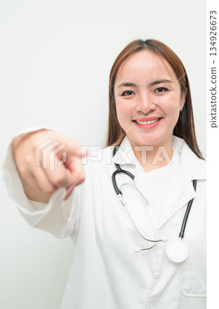Portrait of young Asian female doctor against white background pointing finger at camera 134926673
