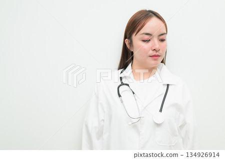 Portrait of young Asian female doctor against white background looking pensive Portrait of young Asian female doctor against white background looking pensive 134926914