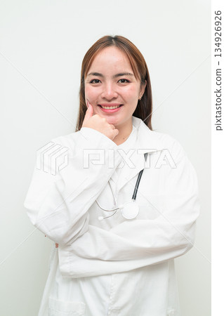 Portrait of young happy Asian female doctor against white background hand on chin thinking Portrait of young happy Asian female doctor against white background hand on chin thinking 134926926