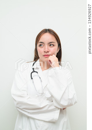 Portrait of young Asian female doctor against white background hand on chin thinking Portrait of young Asian female doctor against white background hand on chin thinking 134926927