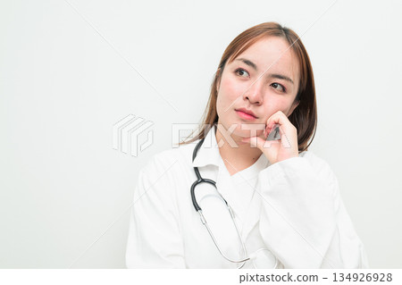 Portrait of young Asian female doctor against white background hand on chin thinking Portrait of young Asian female doctor against white background hand on chin thinking 134926928